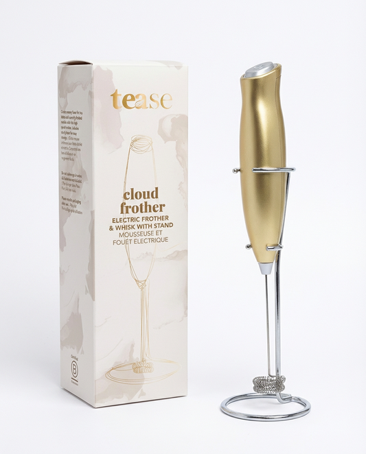 Gold-toned electric frother with sleek design and matching stand next to beige packaging box.